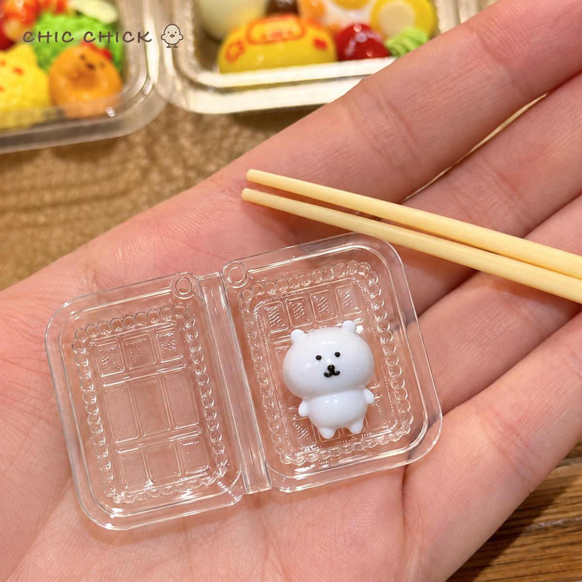 Hand holding the open clear box with the white bear squishy
